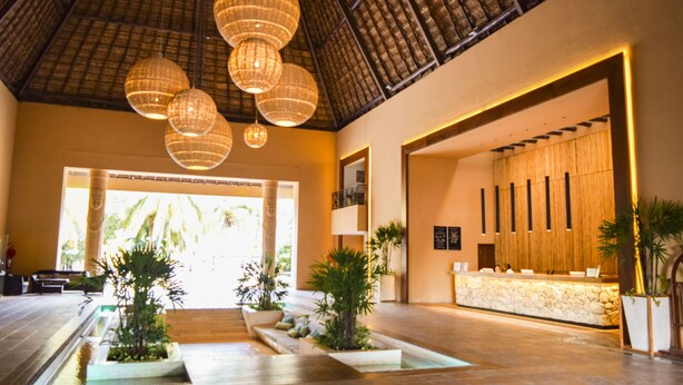 A spacious lobby with a reception desk, multiple potted plants, and a high ceiling with hanging lamps. - Reef Yucatan Hotel and Convention Center All Inclusive (Telchac Puerto)