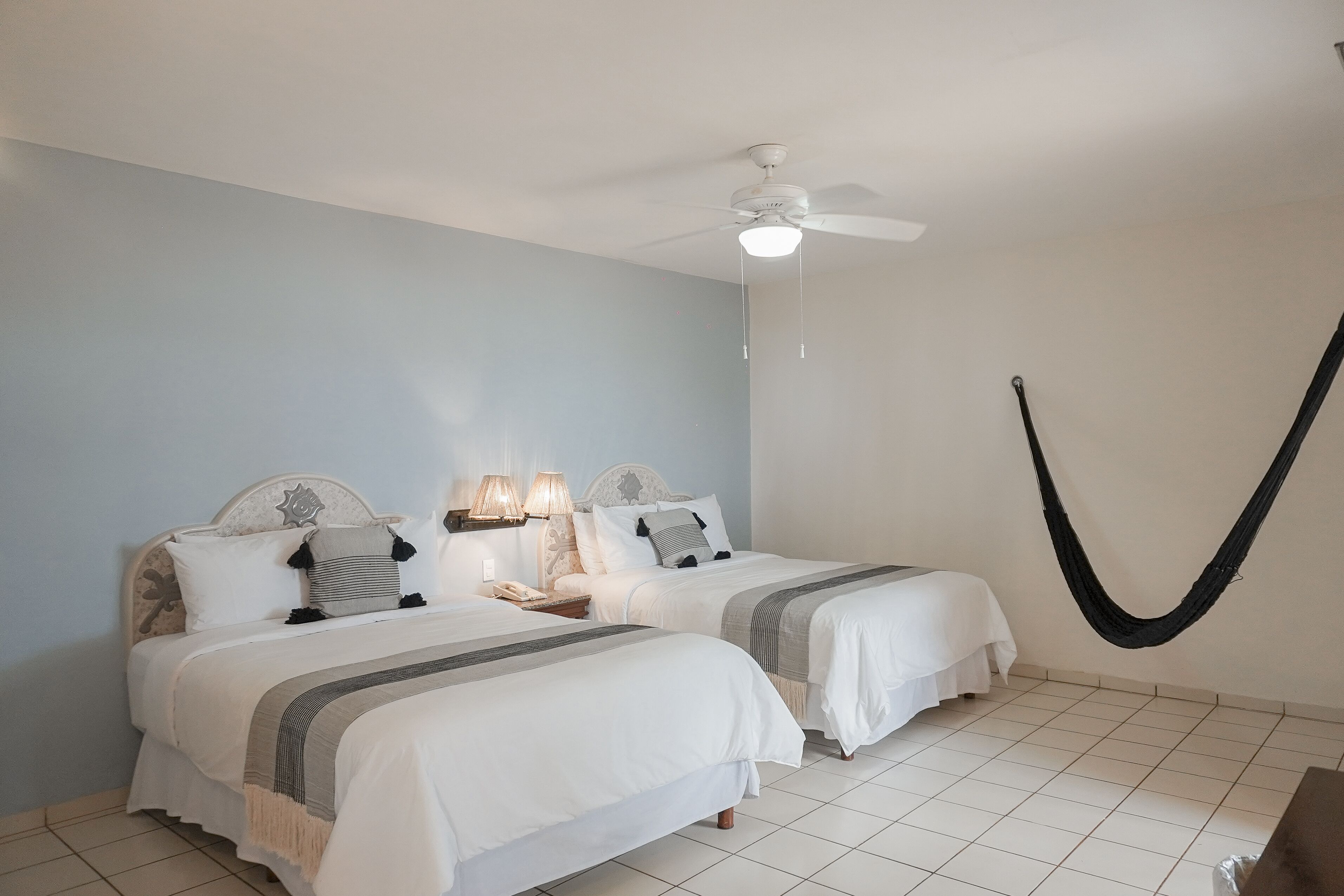 A bedroom with two beds, a ceiling fan, bedside lamps, and a hammock.