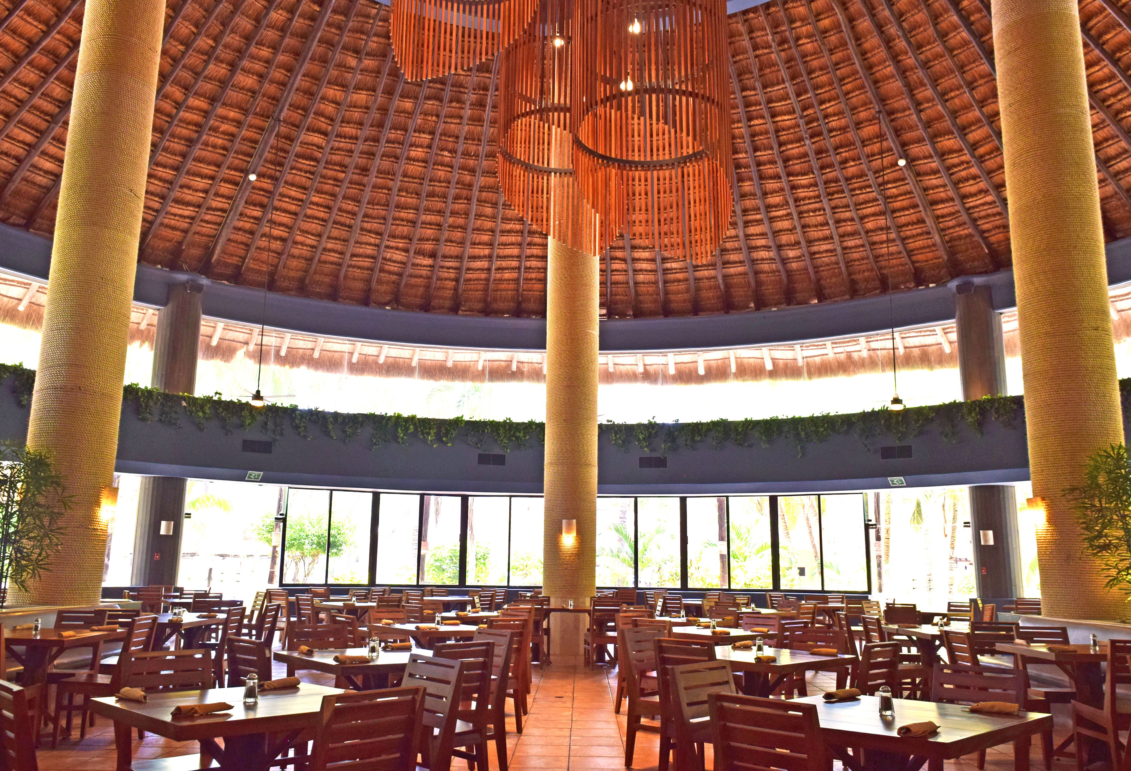 A spacious indoor dining area with high ceilings, large windows, and wooden tables and chairs.