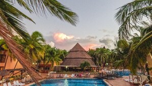 A pool area with lounge chairs and a thatched-roof structure. - Reef Yucatan Hotel and Convention Center All Inclusive (Telchac Puerto)