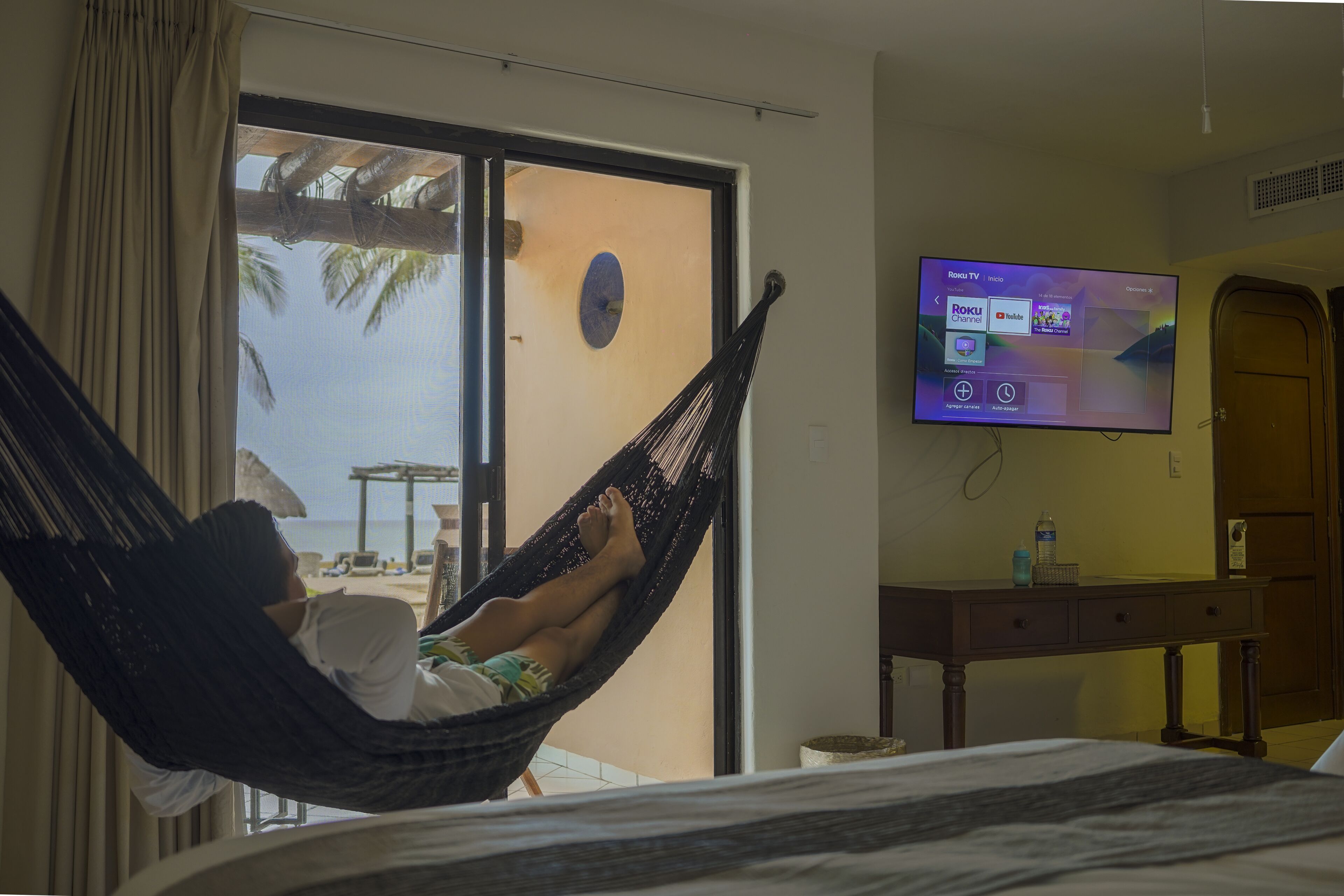 A room with a bed, a TV on the wall, a desk, and a window with curtains.