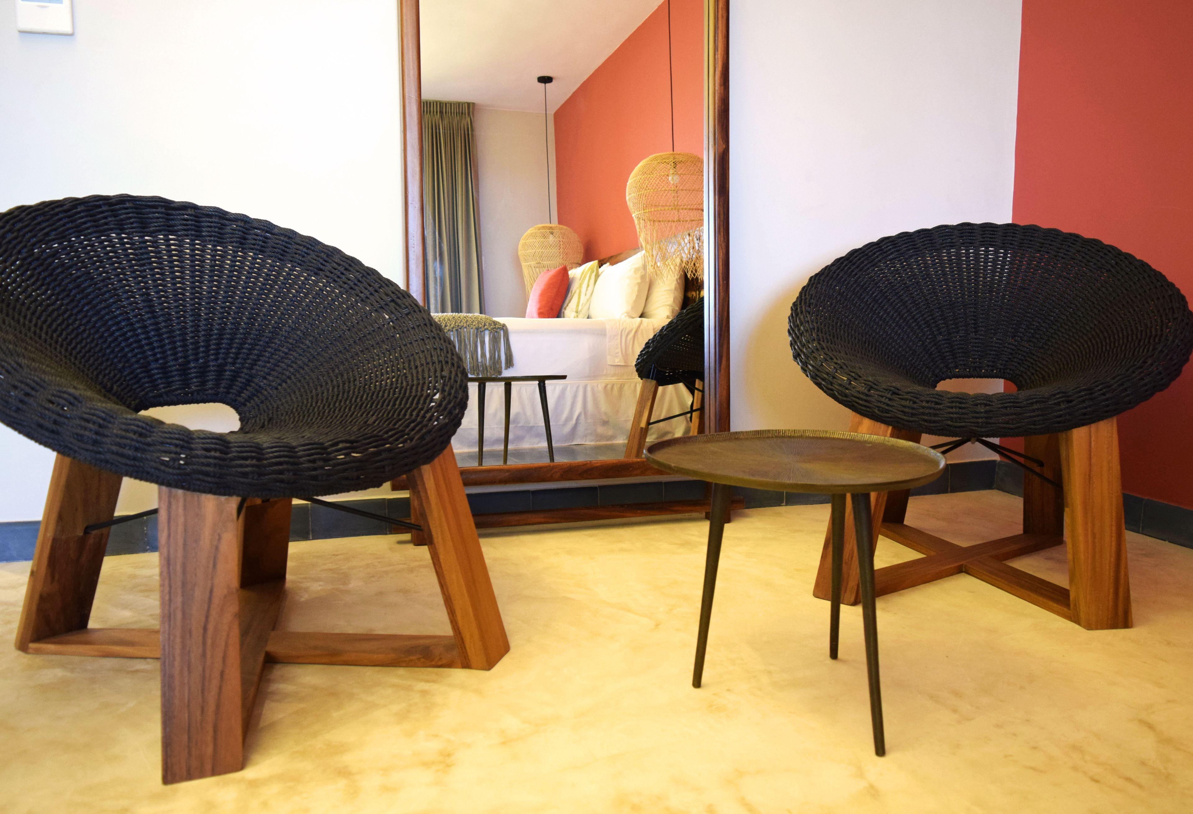 Ein Zimmer mit zwei schwarzen Korbstühlen, einem kleinen runden Tisch und einem Bett, an dessen Wand eine rote Farbe und weiße Vorhänge zu sehen sind.