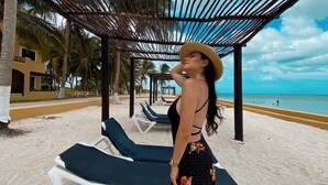 A beachside lounge area with sun loungers under a wooden pergola, palm trees, and a clear view of the ocean. - Reef Yucatan Hotel and Convention Center All Inclusive (Telchac Puerto)