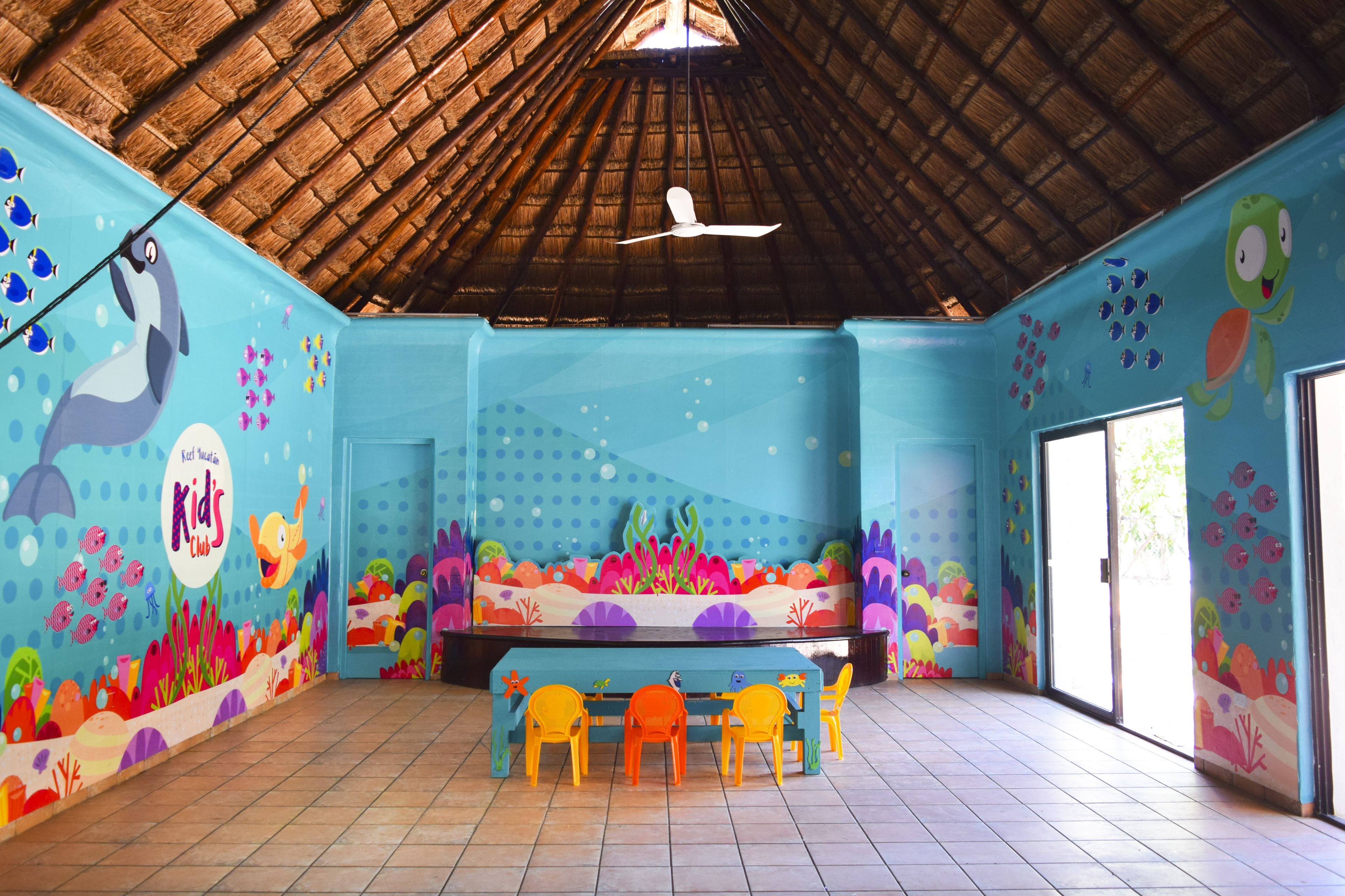 Ein Kinderspielbereich mit Wandgemälde, Deckenventilator und Tisch mit Stühlen.