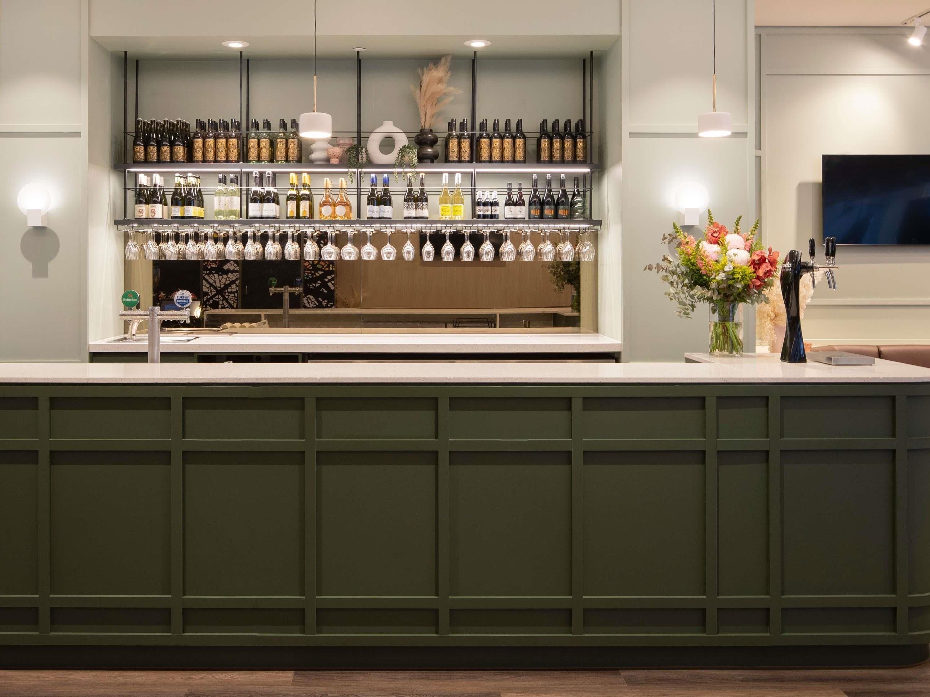 Una zona de bar con estanterías llenas de botellas, un soporte para copas de vino y un florero.