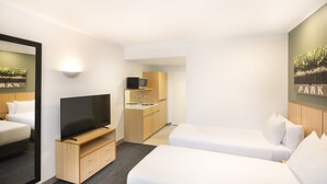 Una habitación de hotel con televisión, cama, kitchenette pequeña y espejo.