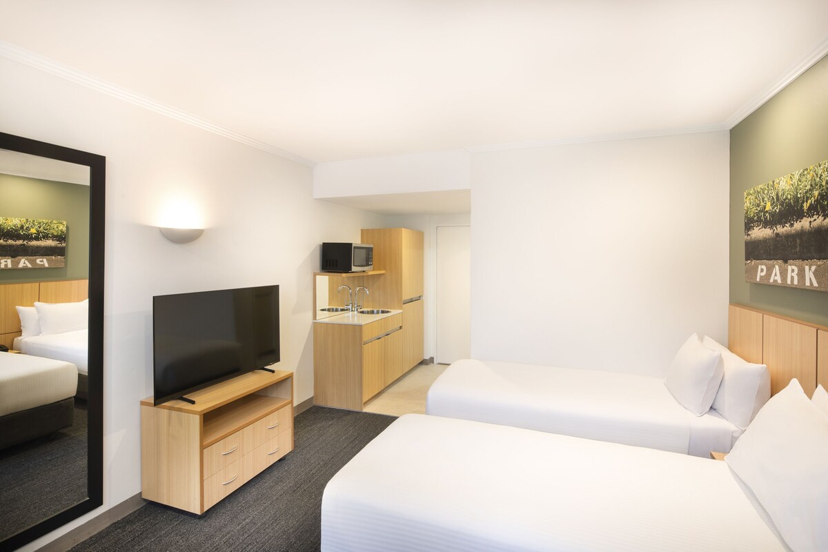 Une chambre d’hôtel équipée d’une télévision, d’un lit, d’une petite kitchenette et d’un miroir.