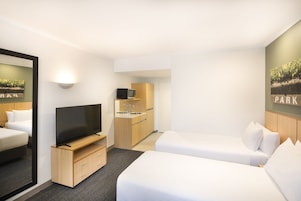 Una habitación de hotel con televisión, cama, kitchenette pequeña y espejo.