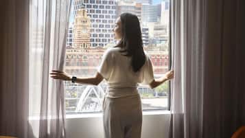 A person standing by a window with a cityscape view, curtains, and a table.