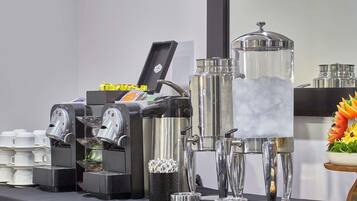 Una estación de café con varias máquinas de café, un dispensador de agua grande y una variedad de alimentos sobre una mesa.