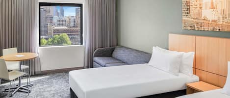 Habitación de hotel con cama, zona de estar, una mesa y vistas a la ciudad.