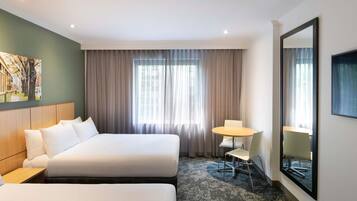 Una habitación de hotel con dos camas, una mesita con sillas, un espejo grande y un cuadro en la pared.