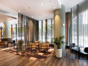 Un hall d’hôtel moderne avec un espace salon, de grandes fenêtres et une plante en pot.
