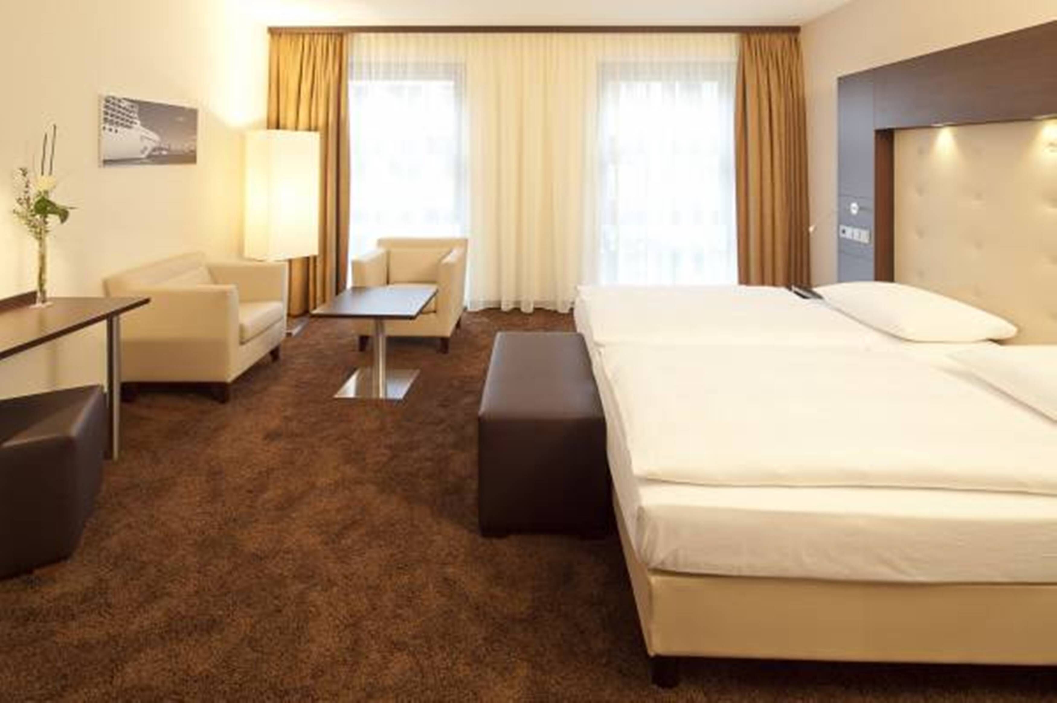 A hotel room with a large bed, a desk, a chair, and a small table.