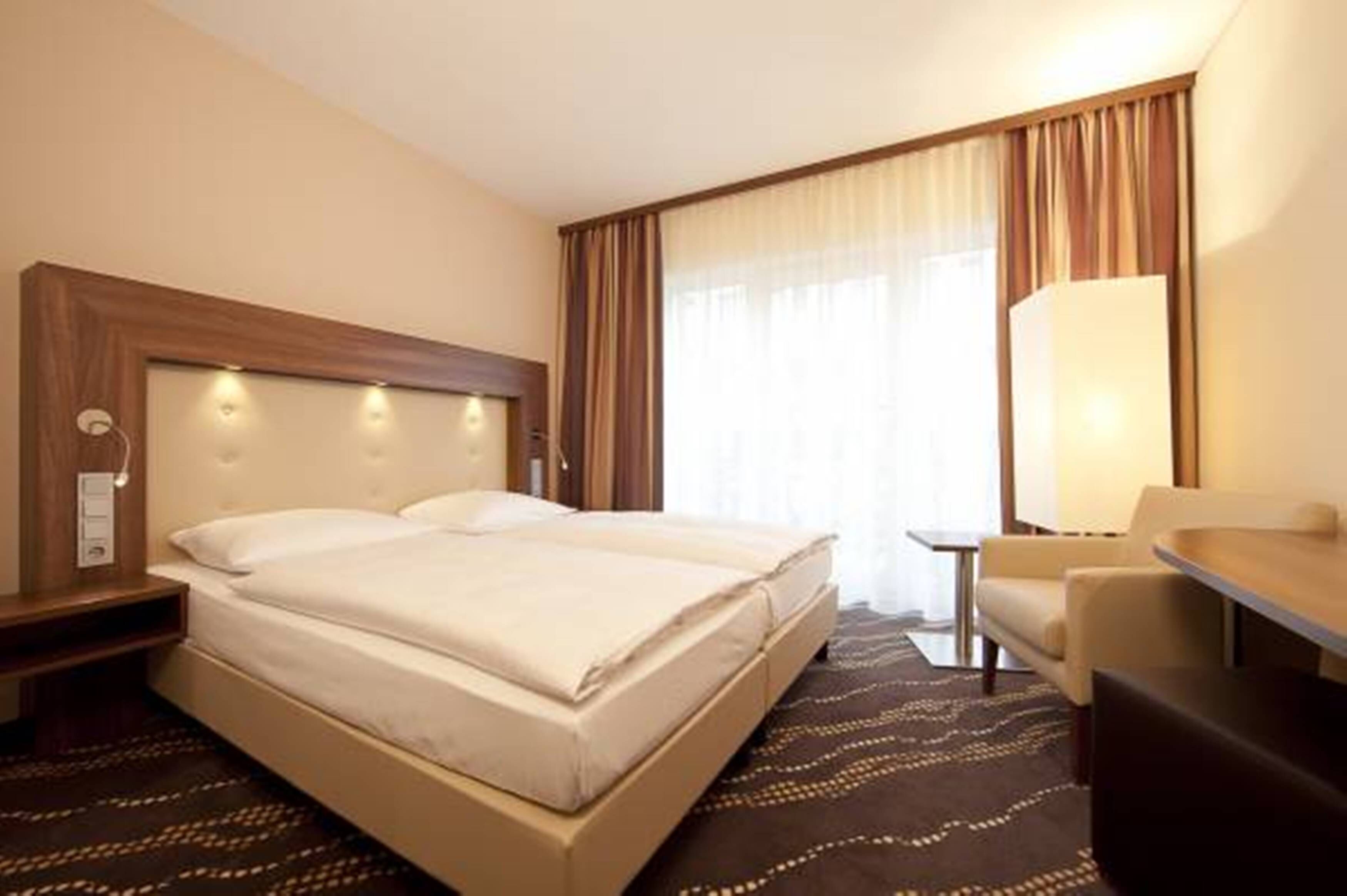 A hotel room with a large bed, a desk, a chair, and a lamp.