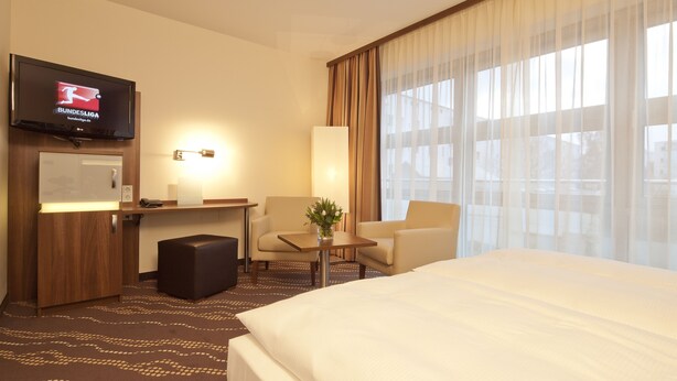 Een hotelkamer met een bed, een bureau, een stoel, een televisie en een raam met gordijnen.