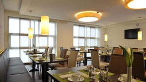 A hotel dining area with multiple tables, chairs, and a television mounted on the wall.