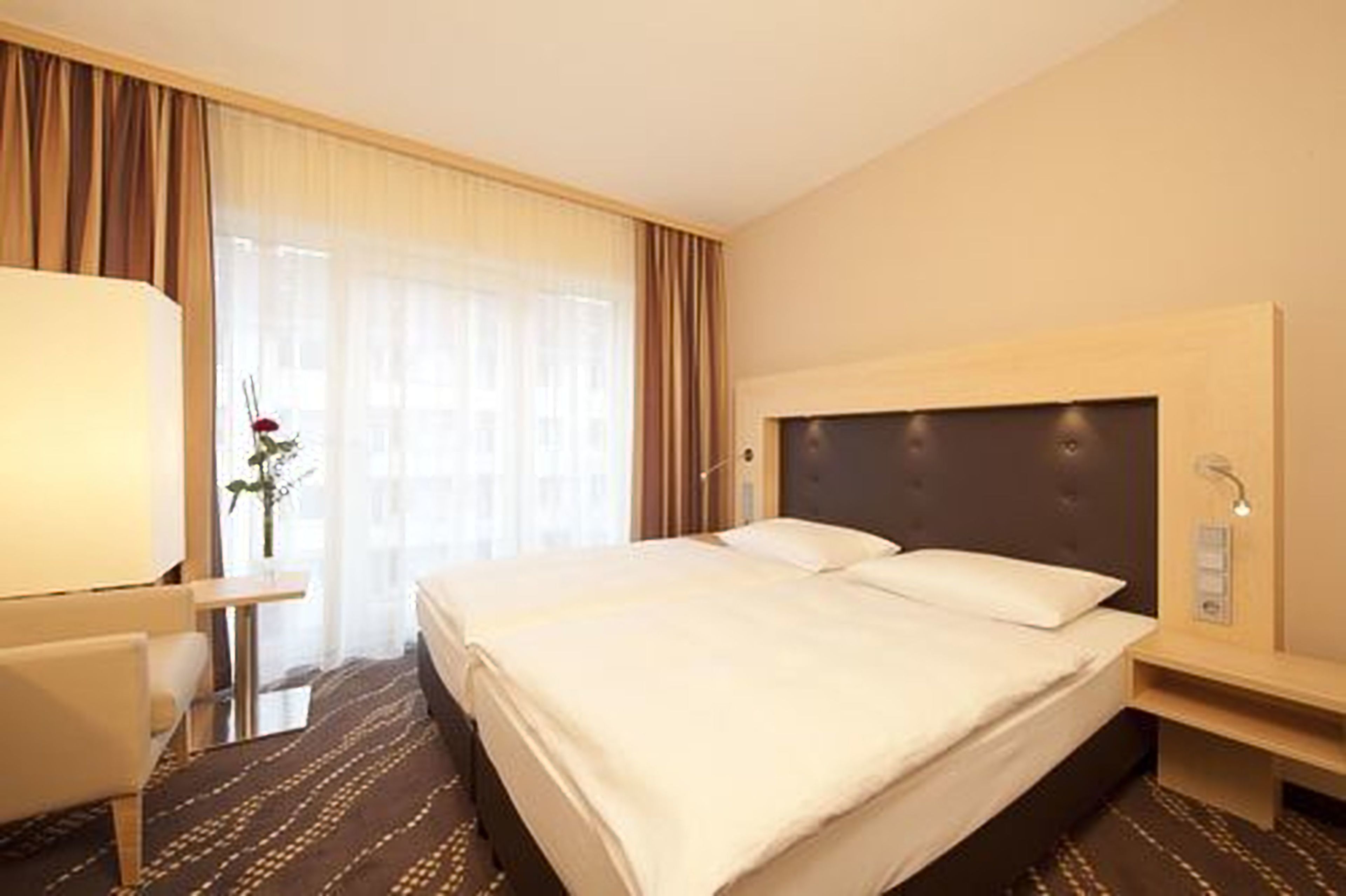 Een hotelkamer met een groot bed, een nachtkastje, een lamp en een raam met gordijnen.