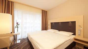 Een hotelkamer met een groot bed, een nachtkastje, een lamp en een raam met gordijnen.