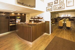 A reception area with a wooden reception desk, a bookshelf with magazines, and framed pictures on the wall. - Heikotel - City Nord (Hamburg)