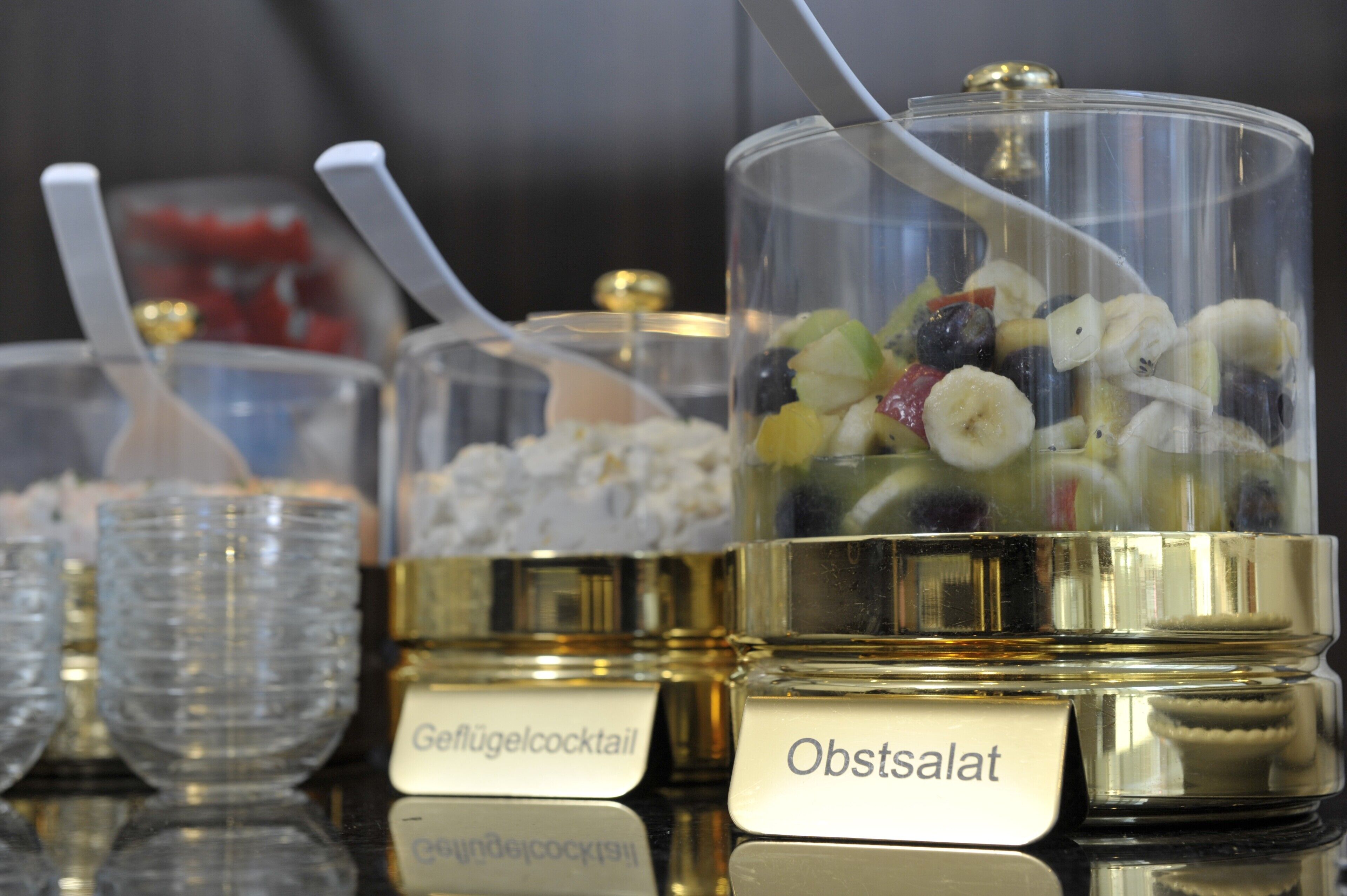 Verschiedene Behälter für Speisen und Getränke mit Etiketten, die unterschiedliche Cocktailarten und einen Salat ausweisen.