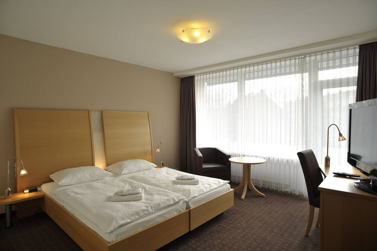 A hotel room with a double bed, a desk with a TV, a chair, and a small table.