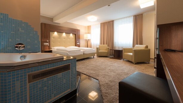 Une chambre d’hôtel avec une grande baignoire, un lit, deux fauteuils, une petite table et un tél éviseur.