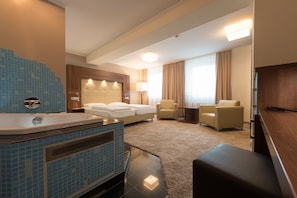 A hotel room with a large bathtub, a bed, two armchairs, a small table, and a television. - Heikotel - City Nord (Hamburg)