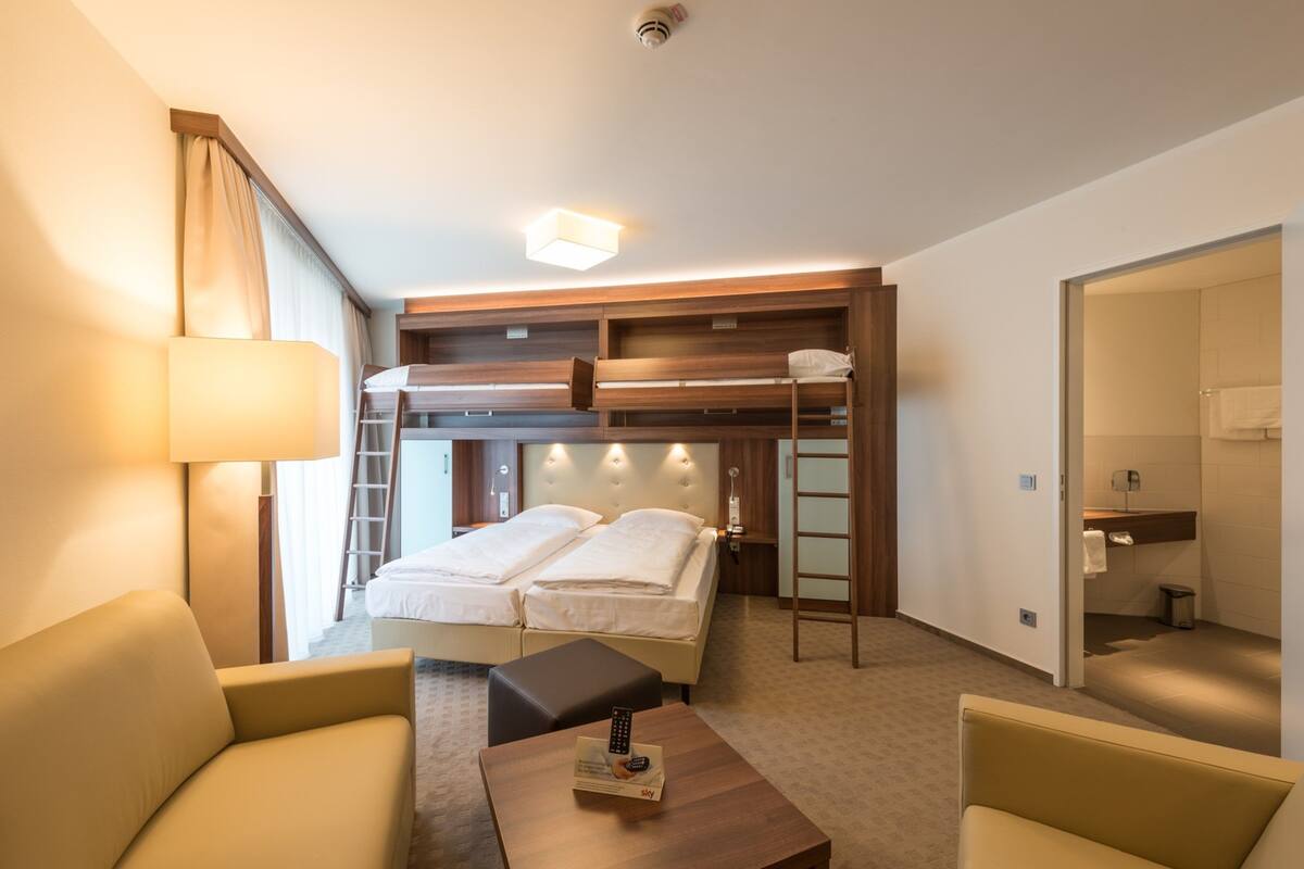 A hotel room with a bed, a desk, a chair, a lamp, a bathroom, and a view of the outside.