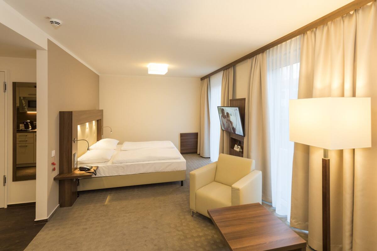 A hotel room with a bed, a chair, a desk, a TV, and curtains.