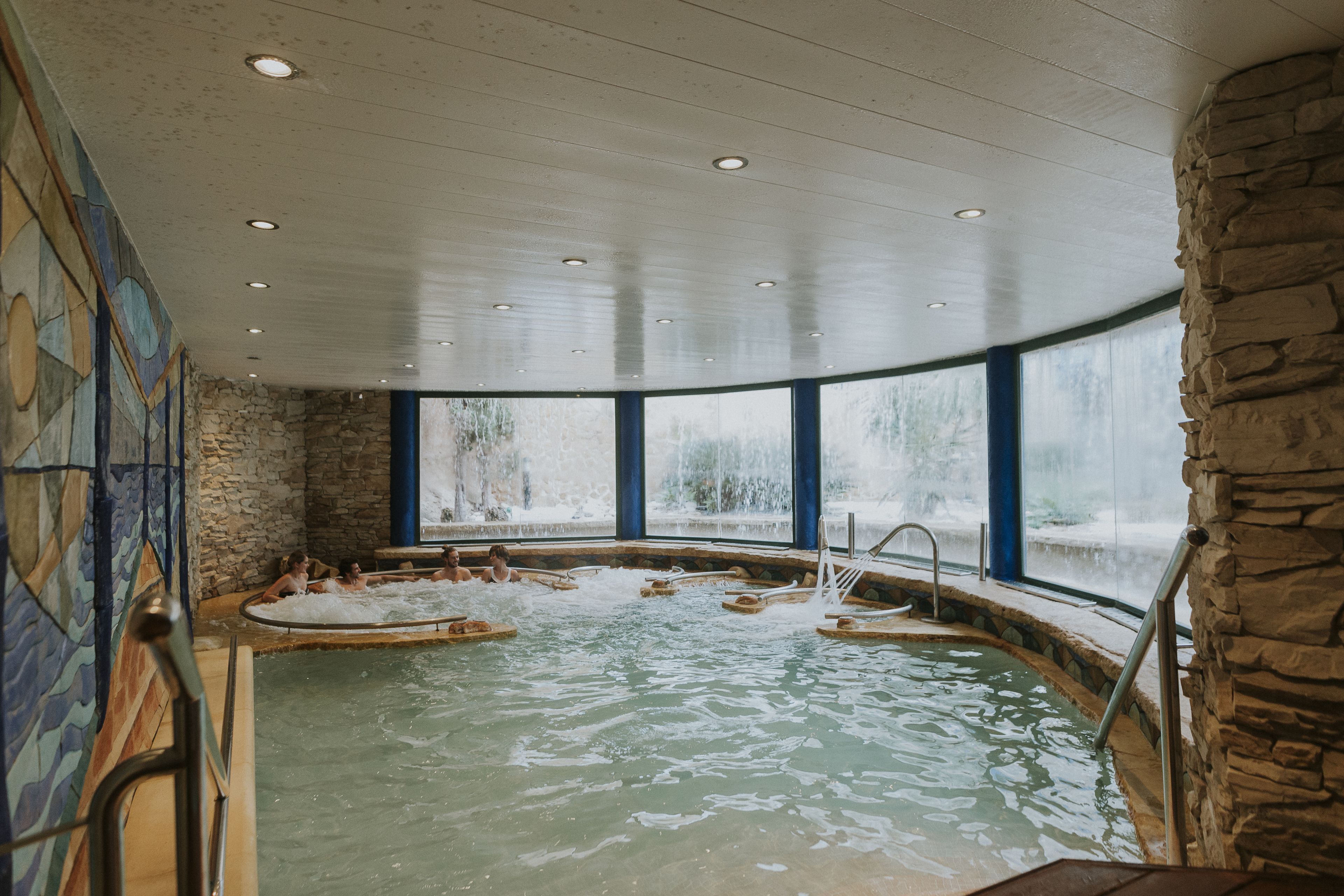 Ein Wellnessbereich mit Steinwand, großem Fenster und Pool mit Stufen.