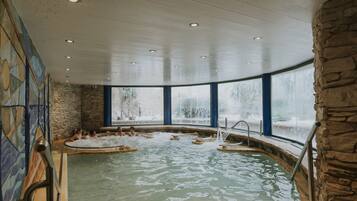 Ein Wellnessbereich mit Steinwand, großem Fenster und Pool mit Stufen.