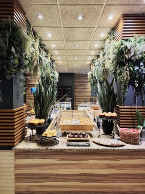 Indulge in a sweet treat at this beautifully designed space, featuring a central display of fresh baked goods and lush greenery.