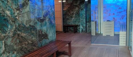 Una habitación con un banco de madera, una pared de mármol y un ventanal de vidrio que da a otra estancia.