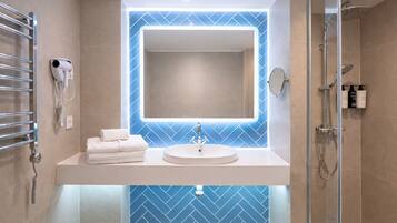 Un baño moderno con un lavamanos blanco, un espejo grande, un secador de pelo de mano y una mampara de ducha de vidrio.