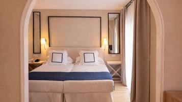 Una cama doble con detalles azules, una mesita de noche con lámpara y un espejo grande sobre la cama.