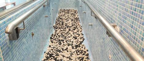 A narrow, tiled corridor with a pebble-lined path, metal handrails, and a view of the outside.