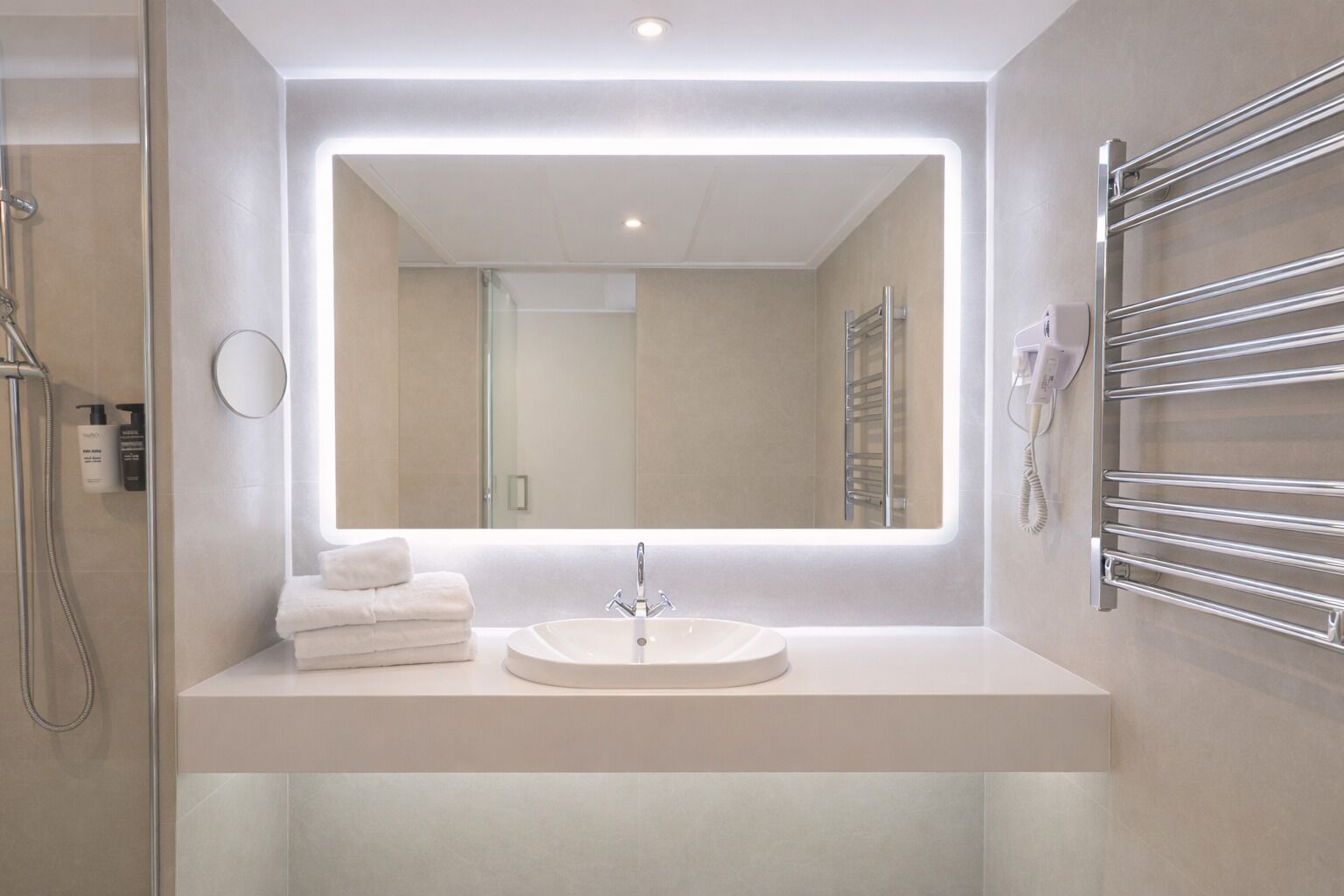 Un baño moderno con un espejo grande, un lavamanos redondo y un perchero para toallas.