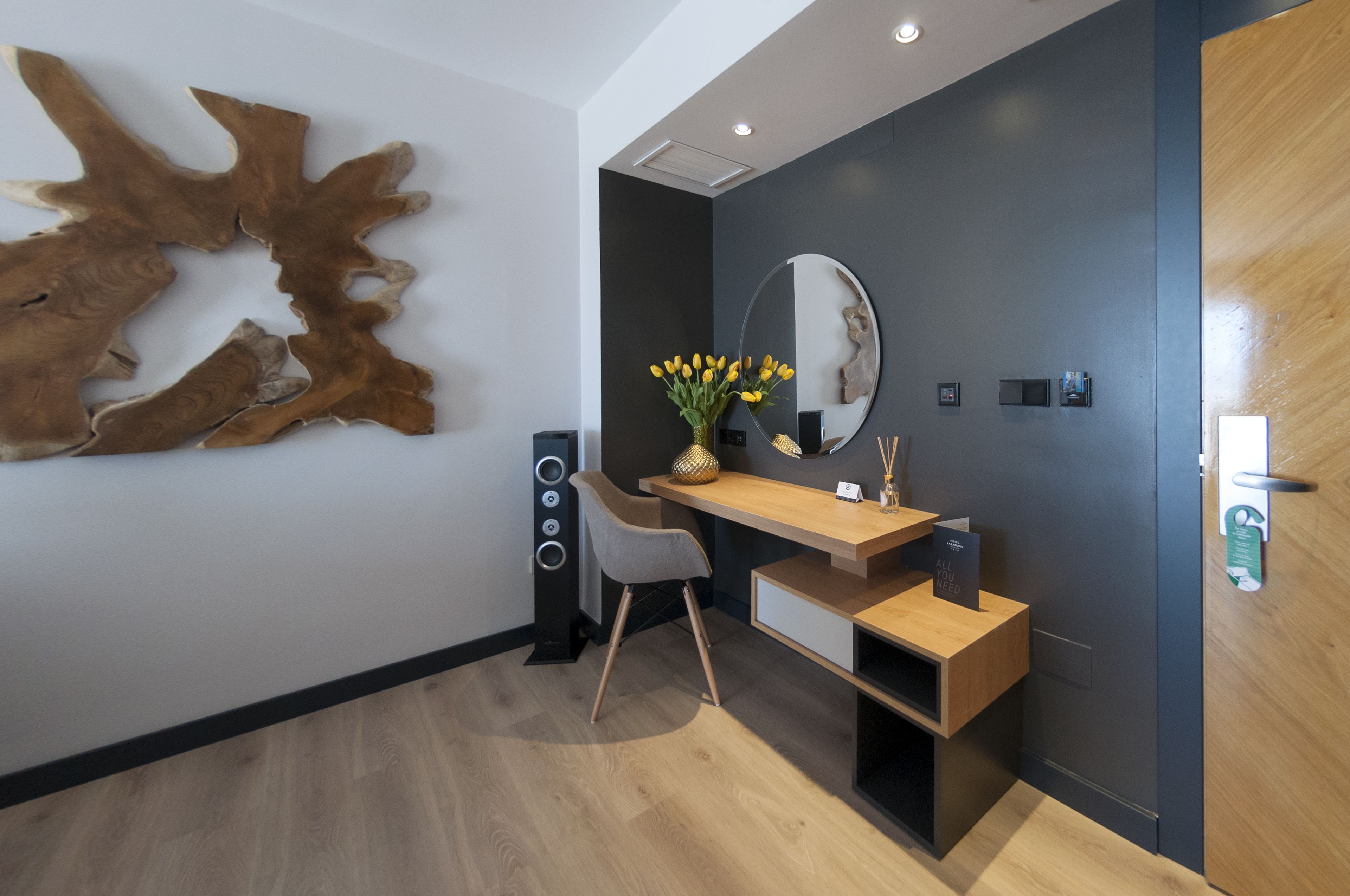 A modern reception area with a wooden desk, a mirror, and a decorative wall piece.
