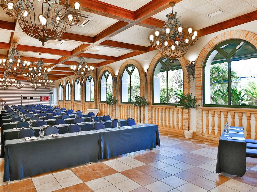 A conference room with rows of tables and chairs, large windows, and multiple chandeliers.