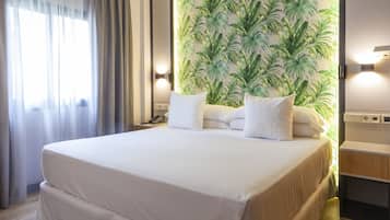 Ein Hotelzimmer mit einem großen Bett, einem Nachttisch mit Telefon, einer Wand mit tropischem Blattmuster und einem Fenster mit Vorhängen.