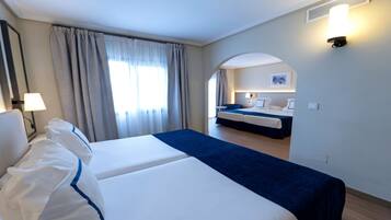 A hotel room with two beds, a sitting area, and a view of the adjacent room.