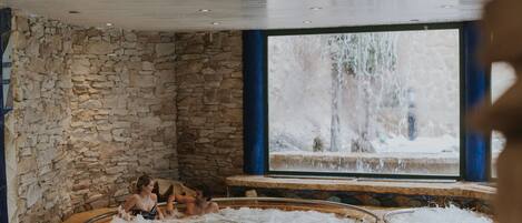 A hot tub area with stone walls and a view of a waterfall outside.