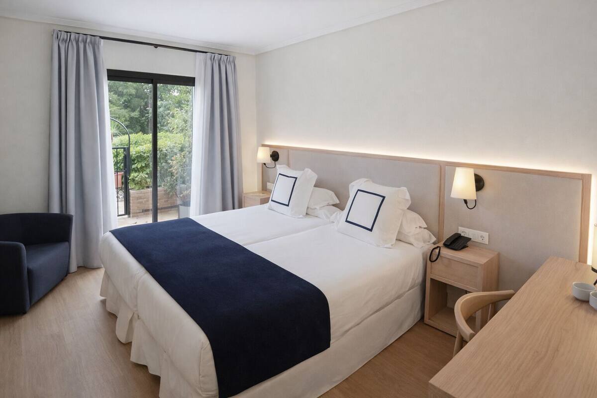 A hotel room with a large bed, a desk, a chair, a phone, and a window with curtains.
