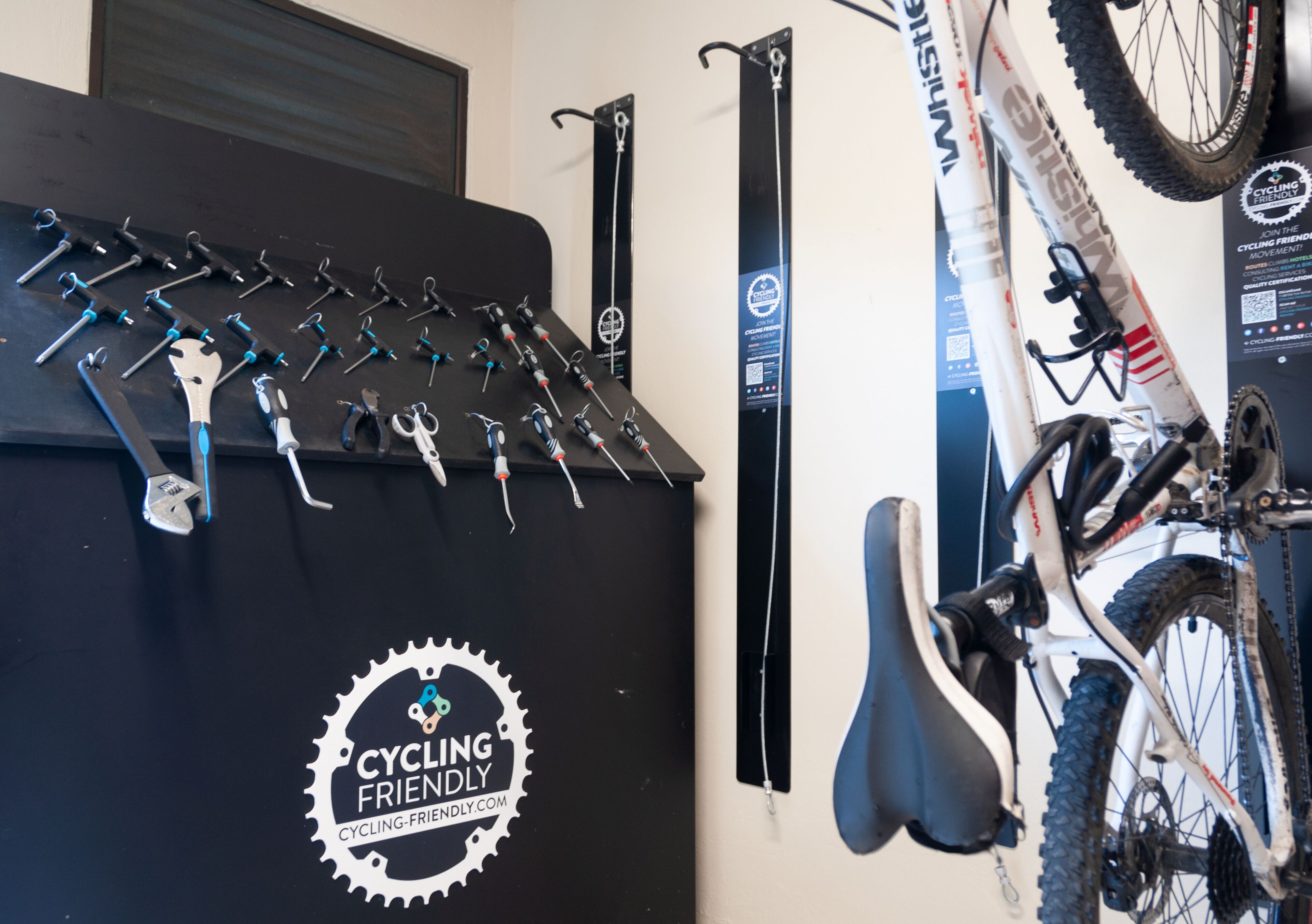 Un porte-vélos fixé au mur, agrémenté de divers accessoires pour cyclistes, un logo indiquant « Espace accueillant pour les cyclistes », et un vélo appuyé contre le mur.