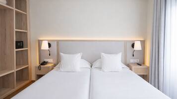 A double bed with white linens, two bedside tables with lamps, a wooden wardrobe, and a neutral-colored wall.