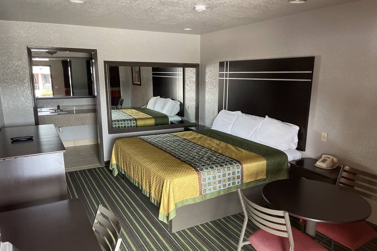 A hotel room with a bed, a desk, a chair, a table, a mirror, and a telephone.