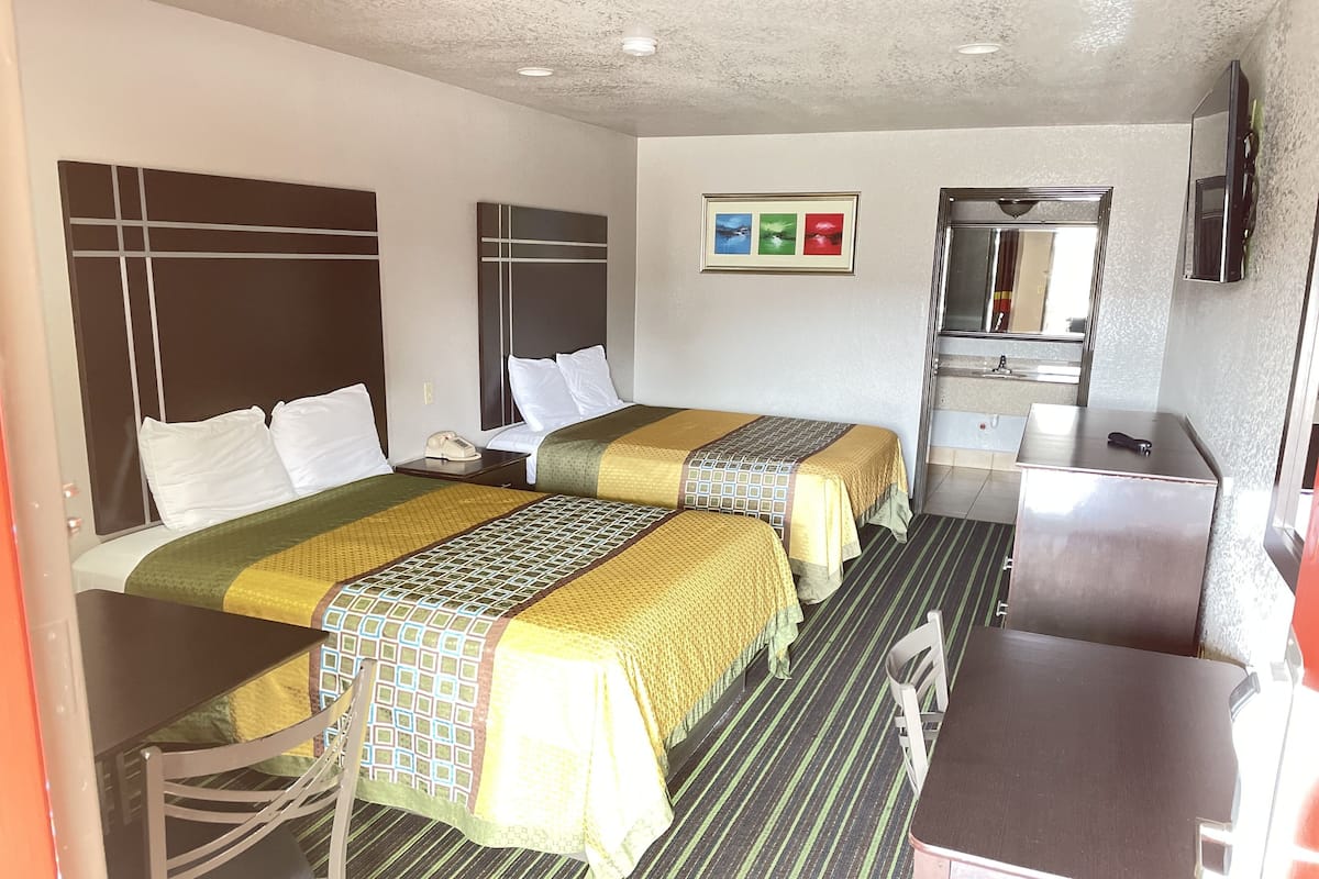 A hotel room with two beds, a desk, a chair, a small table, a mirror, and a picture on the wall.