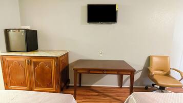 Una habitación con un armario de madera, un televisor montado en la pared, un escritorio de madera, una silla de cuero y dos camas con sábanas blancas.