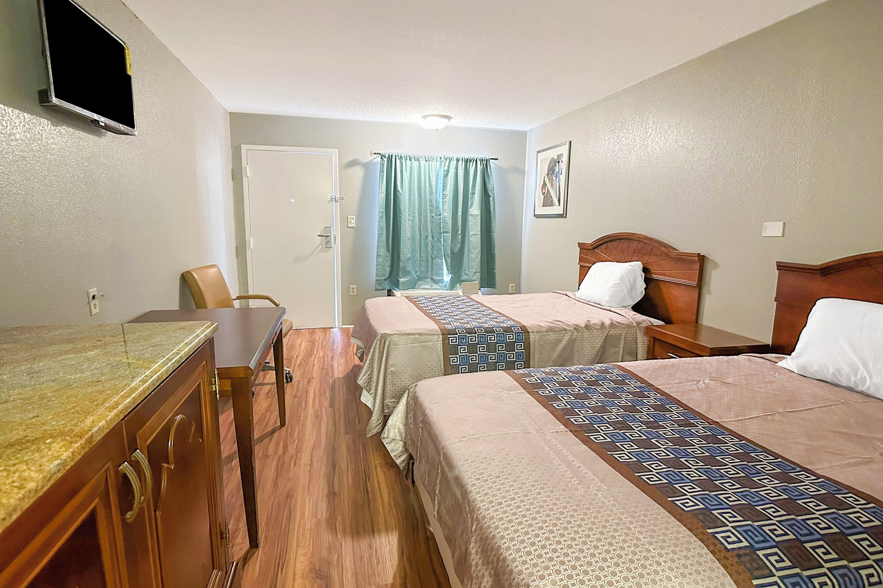 Habitación de hotel con dos camas, un escritorio, una silla y un televisor en la pared.